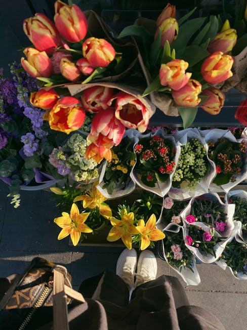 A top-down view of a display of fresh flower bouquets arranged on a dark surface, featuring a variety of floral arrangements with vibrant colours. The bouquet at the top contains pink and orange tulip
